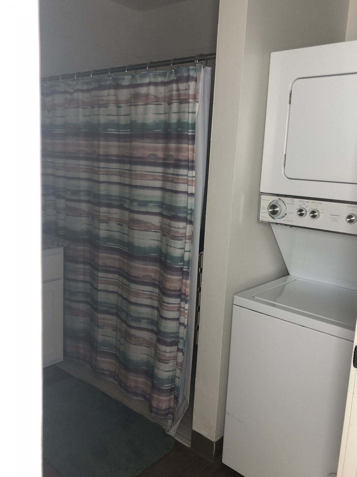 A laundry area with a stacked washer and dryer next to a patterned curtain.