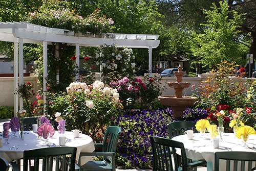 A charming outdoor dining area surrounded by vibrant flowers and a fountain.