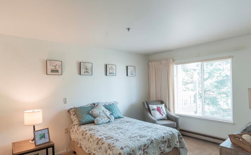 A cozy bedroom with a bed, decorative pillows, and a chair by the window.