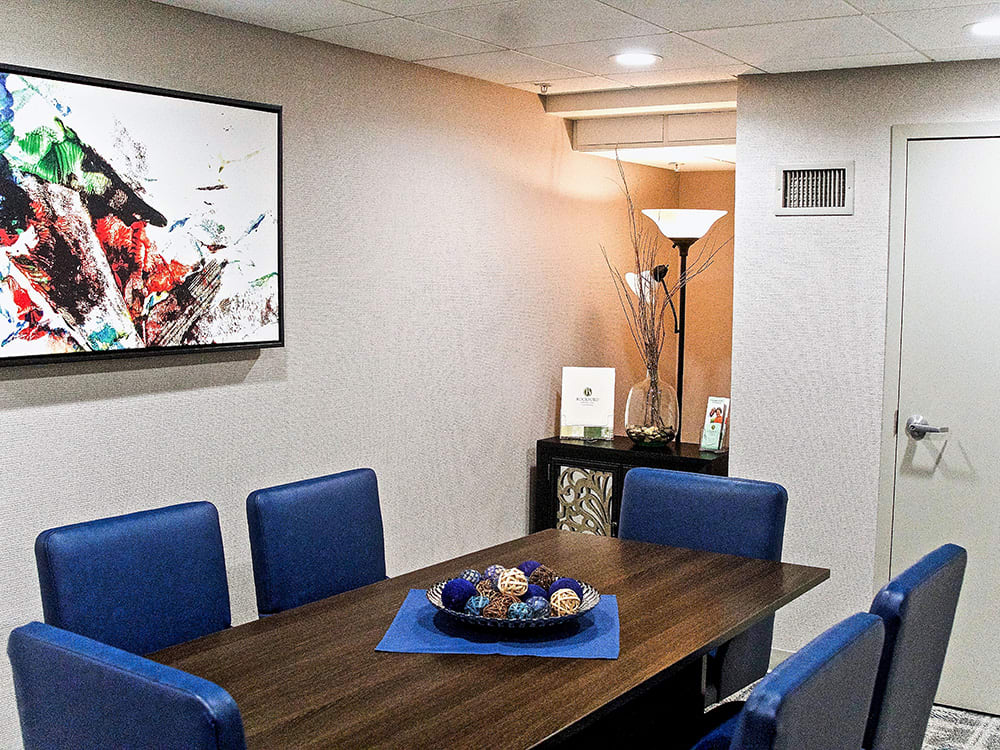A modern dining room with blue chairs, a wooden table, and abstract wall art.