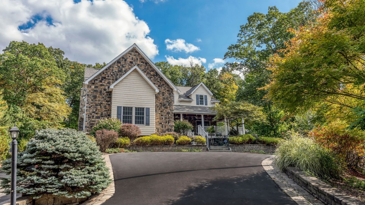 A beautiful house with a stone facade surrounded by lush landscaping and a clear blue sky.