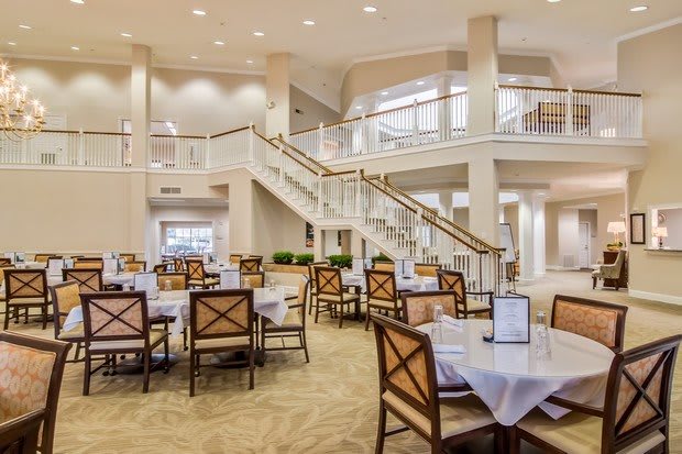A spacious and elegant dining area with neatly arranged tables and chairs, featuring a prominent staircase.