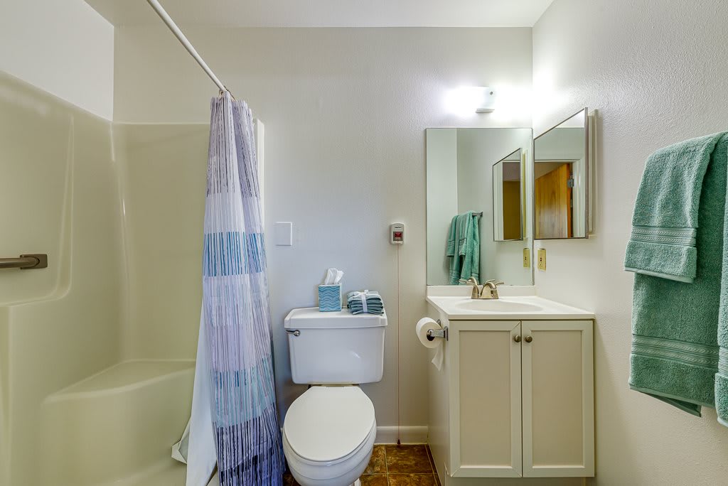 A clean and simple bathroom with a toilet, sink, mirror, and shower area.