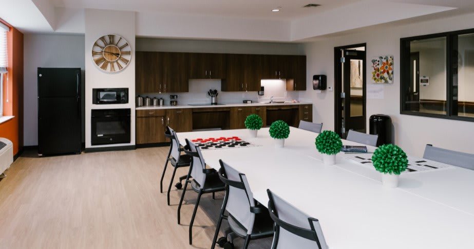 A modern conference room with a large table, chairs, and a kitchenette in the background.