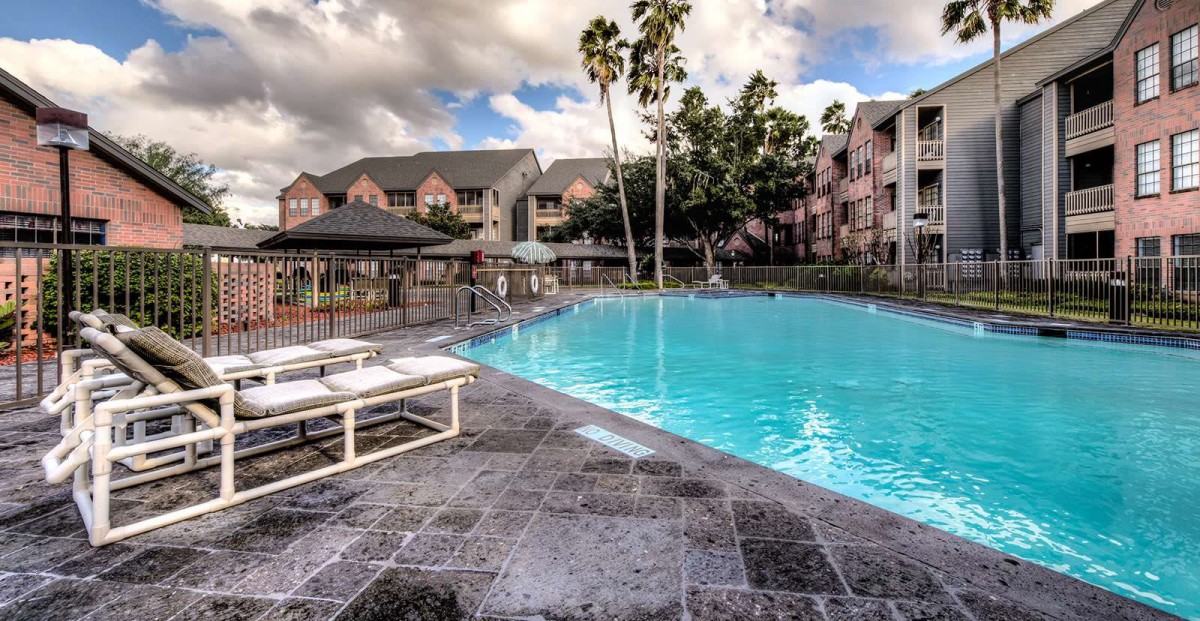 A serene outdoor swimming pool surrounded by apartment buildings and palm trees.