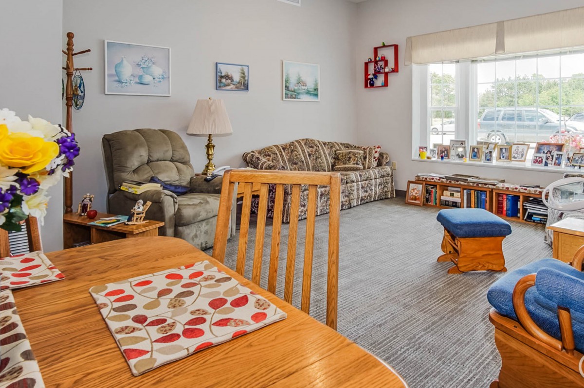 A cozy living room featuring a sofa, reclining chair, and dining table with decor and natural light from a window.