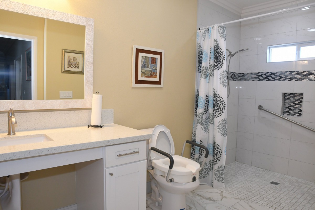 A bathroom with an accessible toilet and a vanity, featuring a shower curtain and wall artwork.