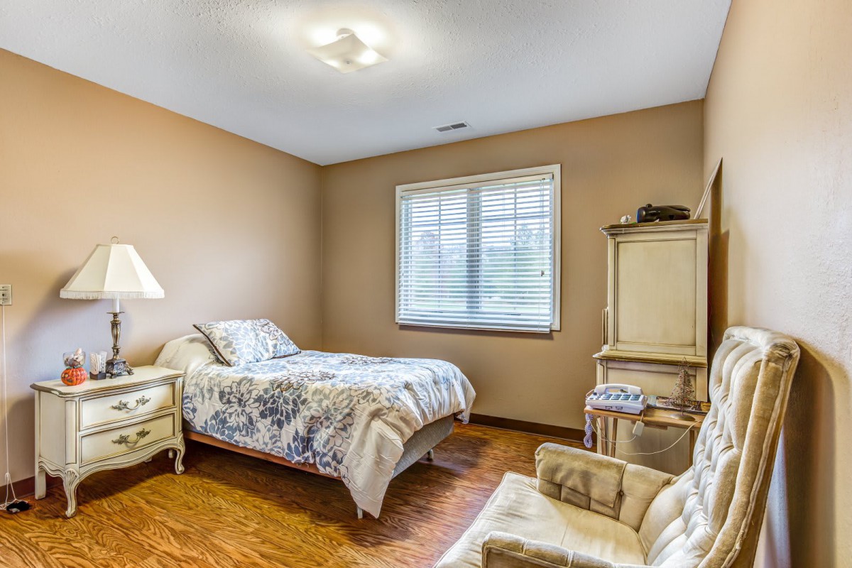 A cozy bedroom with a single bed, lamp, and comfortable chair.