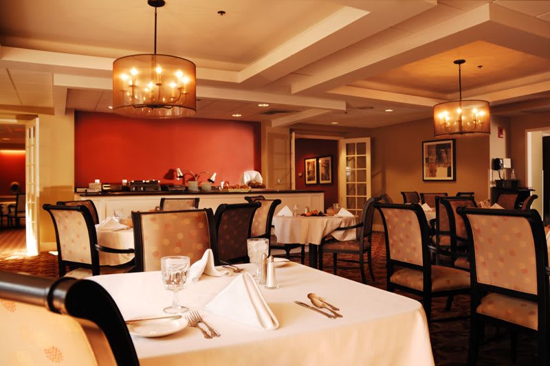 An elegant restaurant dining room with neatly set tables and warm lighting.