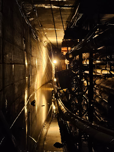 An underground tunnel illuminated by artificial light, showcasing industrial elements and water reflections.