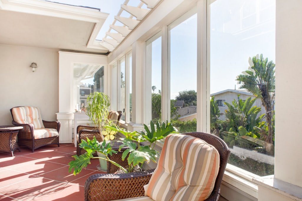 A bright sunroom with comfortable seating and lush greenery, offering an inviting outdoor view.