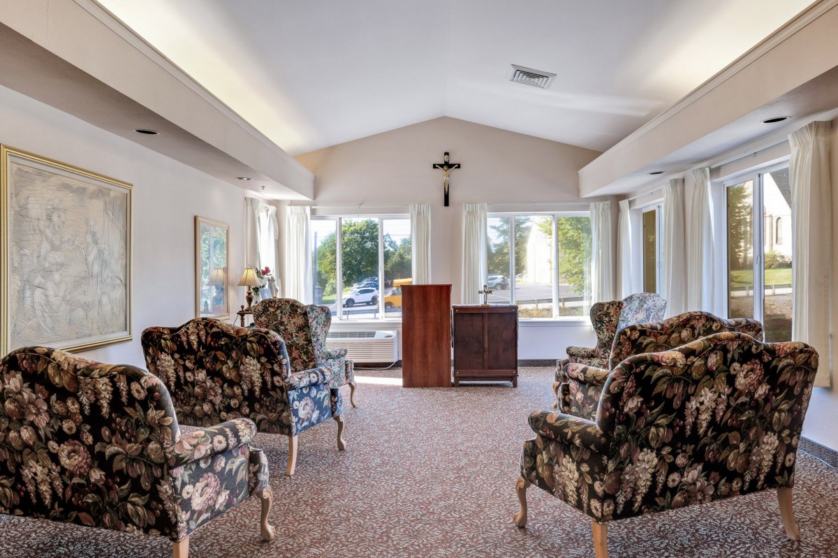 A well-lit living room with floral patterned chairs arranged around a central wooden cabinet.