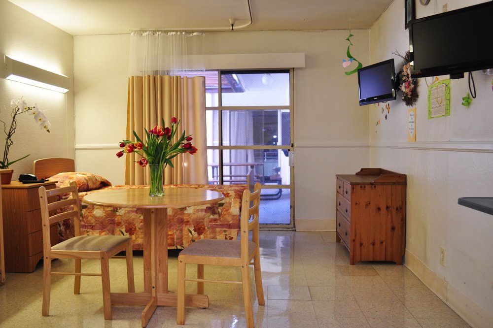 A cozy dining area in an apartment featuring a wooden table with chairs, a television mounted on the wall, and a vase of flowers as a centerpiece.