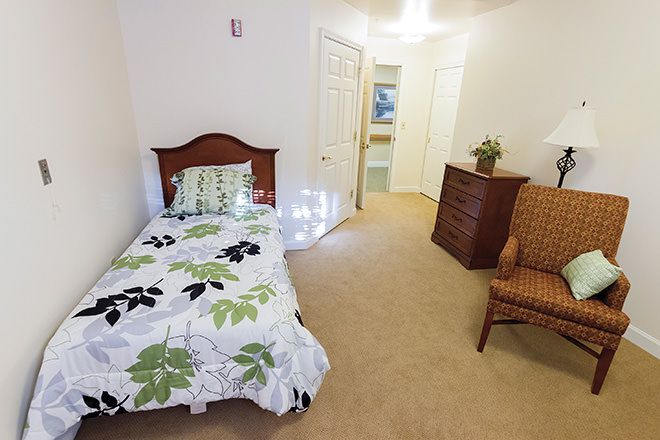 A cozy bedroom with a single bed, dresser, and armchair.