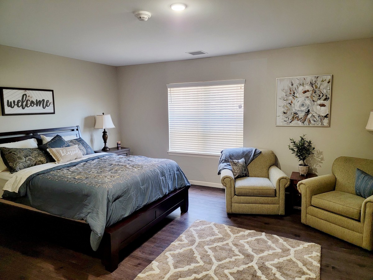 A cozy bedroom with a bed, two armchairs, and a large window letting in natural light.