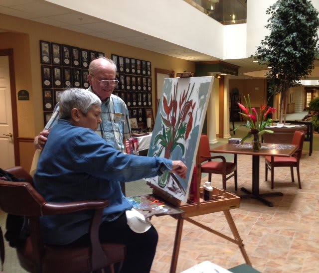 Two elderly individuals engaging in a painting activity indoors.