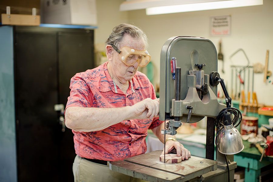 A person operates a drill press in a workshop while wearing safety goggles.