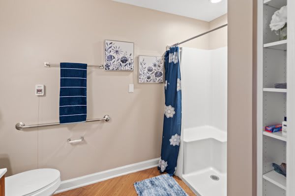 A modern bathroom with blue and white dcor, featuring a shower with a floral curtain, coordinating towels, wall art, and a bath mat.