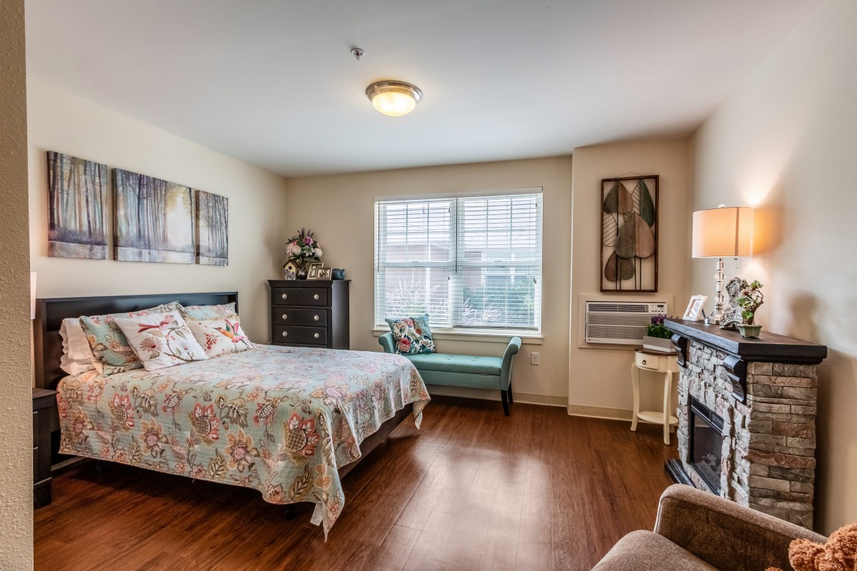 A cozy bedroom with a neatly made bed, decorative furniture, and a well-lit window.