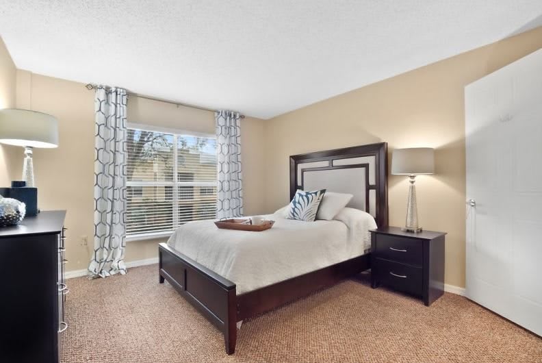 A cozy bedroom with a neatly made bed, nightstand, and lamp by the window.