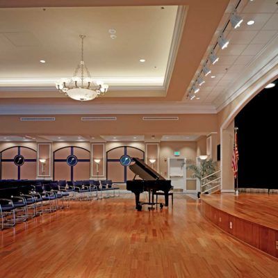 A spacious concert hall featuring a grand piano on stage with elegant seating and a chandelier.