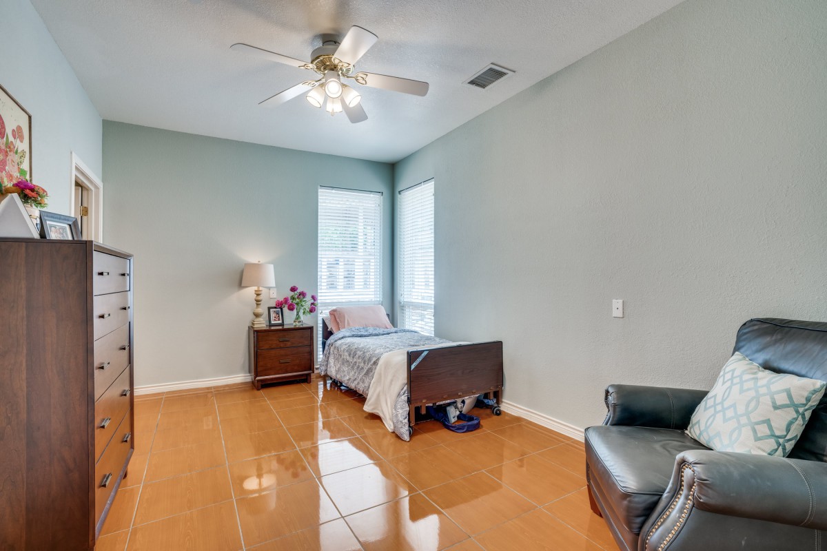 A minimalist bedroom with a single bed, nightstand, and wooden flooring, illuminated by natural light from the windows.