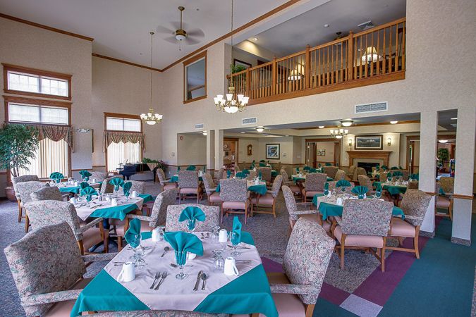 A well-lit dining area with neatly arranged tables and chairs, featuring teal accents and a loft above.