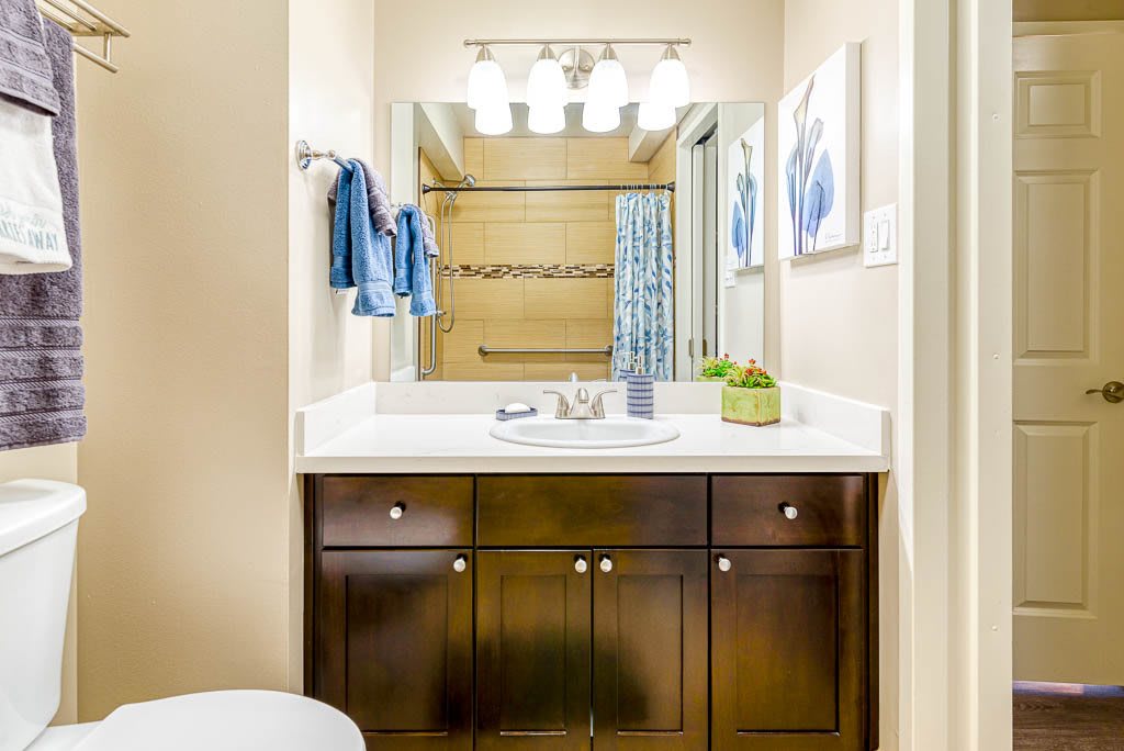 A modern bathroom featuring a dark wood vanity with a sink, mirror, and stylish lighting. Blue towels and decor add a pop of color.