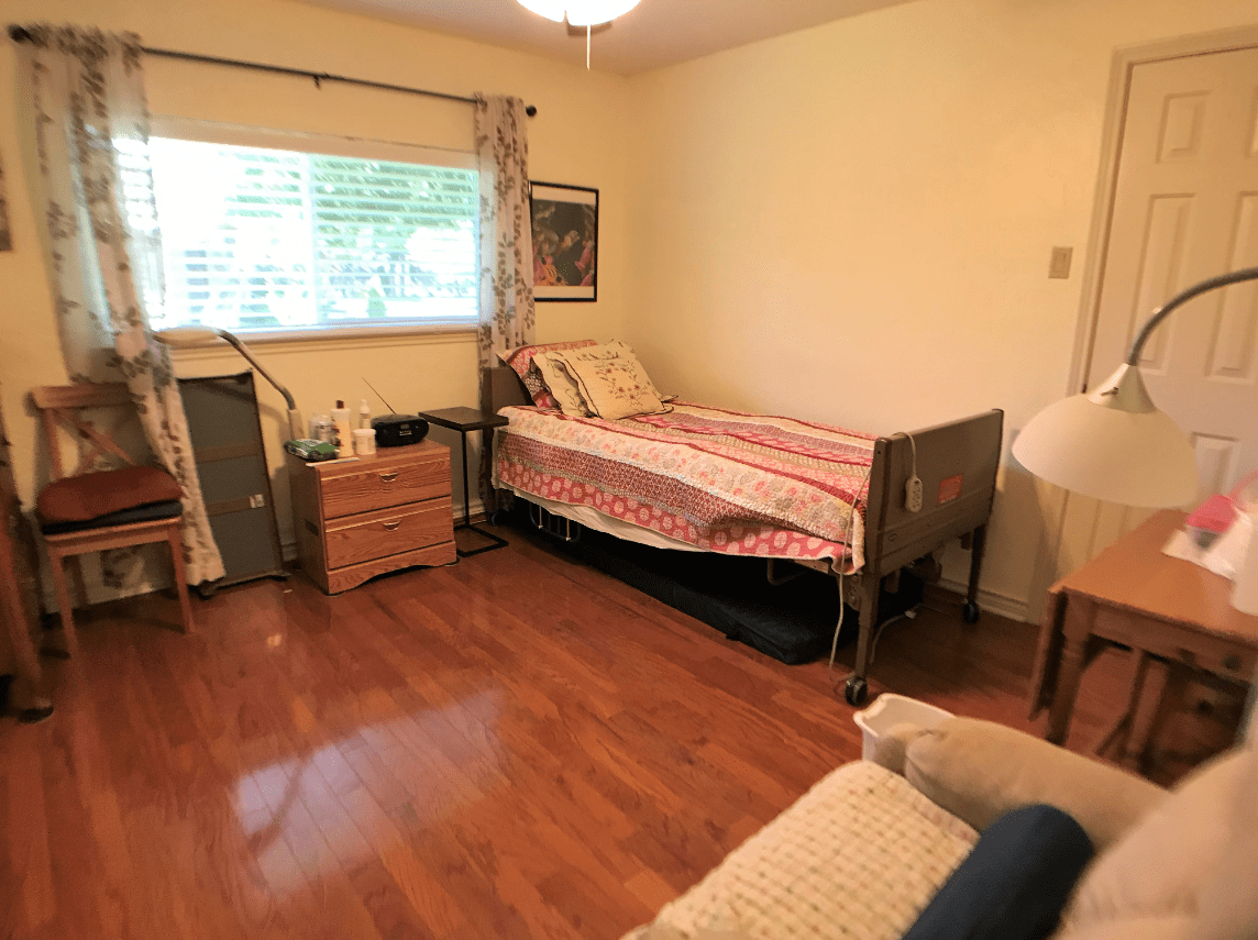 A cozy bedroom with a single bed, wooden flooring, and a window with curtains.