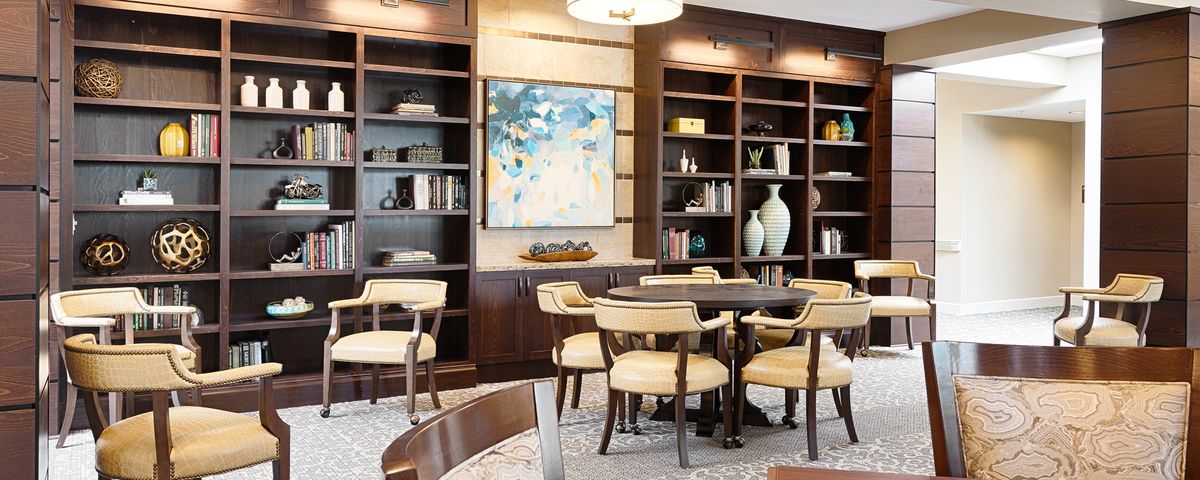 A modern library interior with bookshelves, a table and chairs, and abstract artwork.