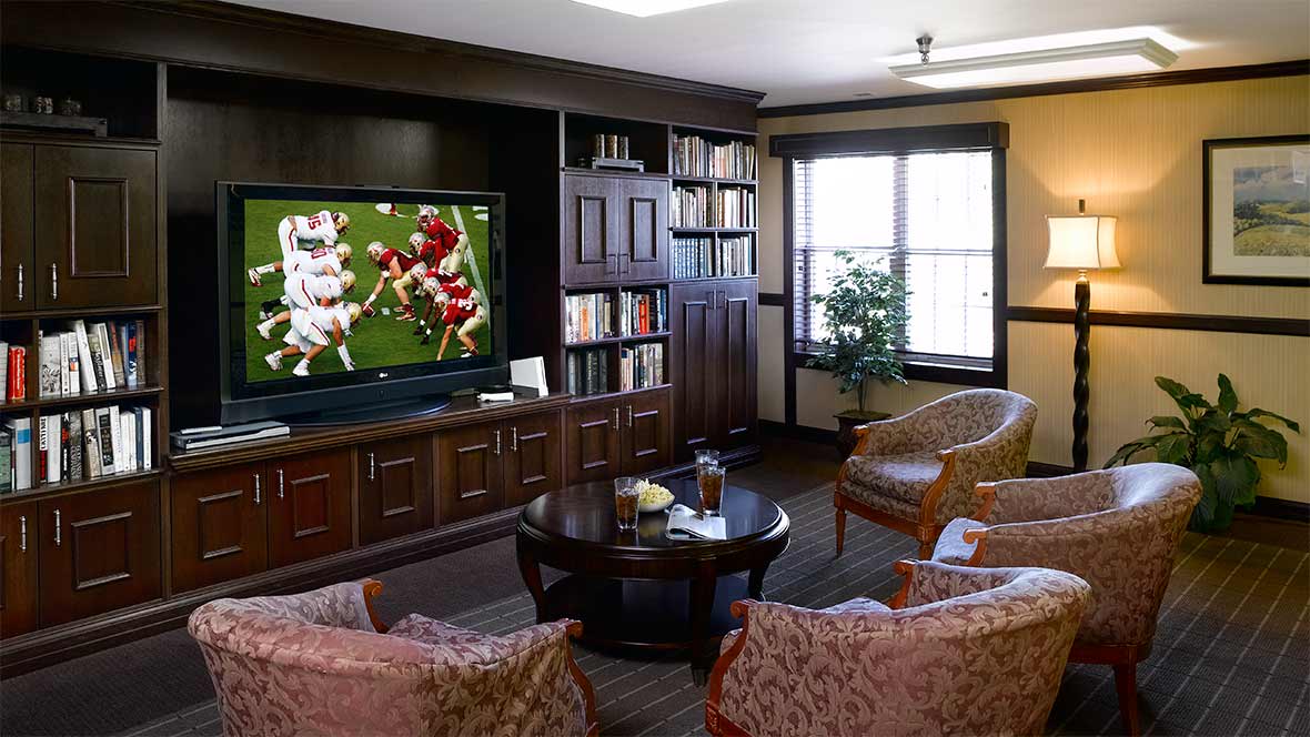 A cozy living room with a television displaying a football game, surrounded by bookshelves and comfortable seating.