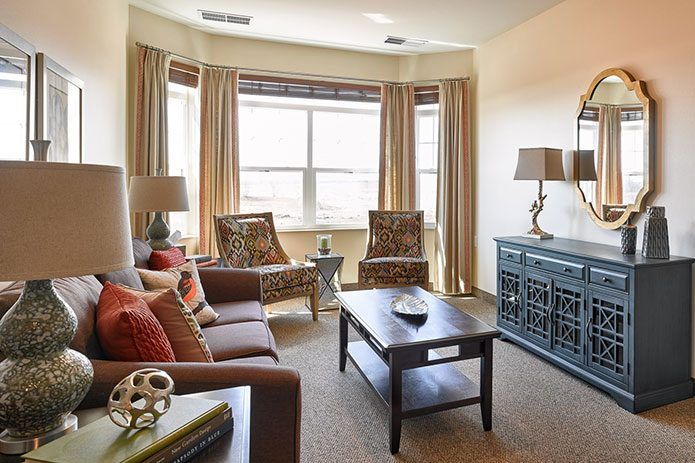 A cozy and beautifully decorated living room with a sofa, patterned chairs, and natural light streaming in through the windows.