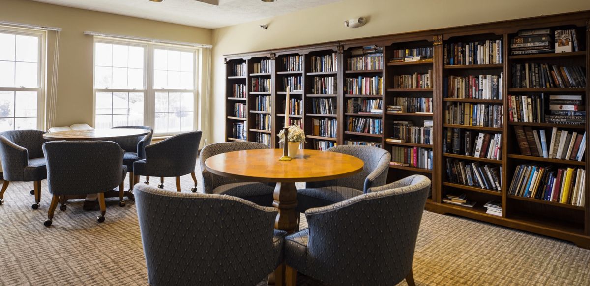 A cozy reading room with a round table surrounded by chairs and lined with bookshelves.