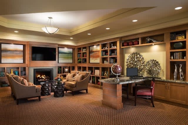 A cozy living room featuring a fireplace, bookshelves, and a home office setup.