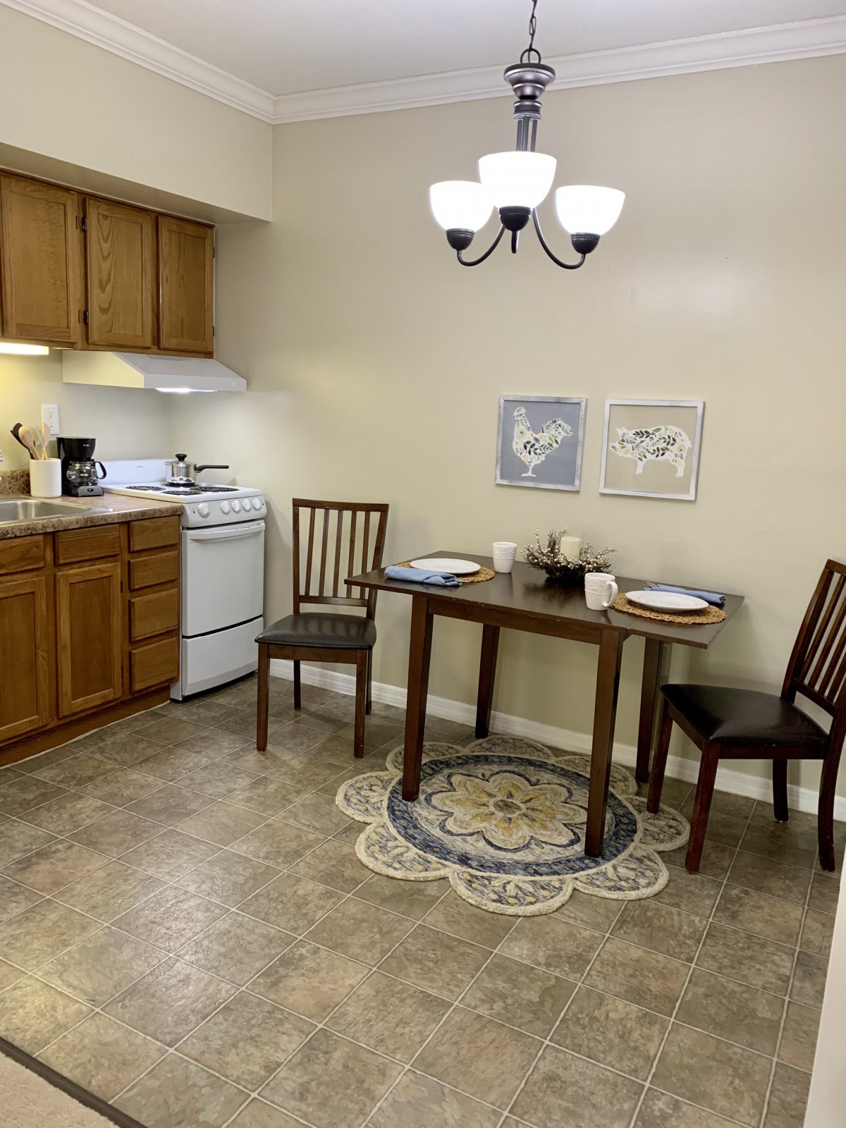 A cozy kitchen with a small dining table set for two, featuring wooden cabinets and a stove in the corner.