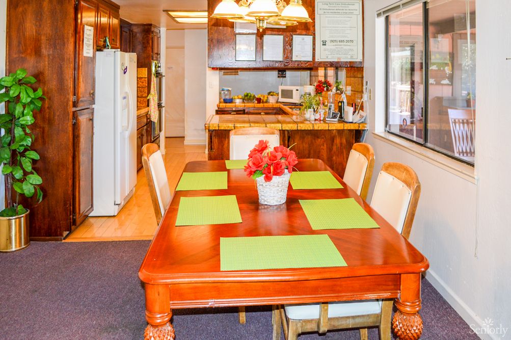A kitchen and dining area with a wooden table set for six, featuring green placemats and a floral centerpiece.