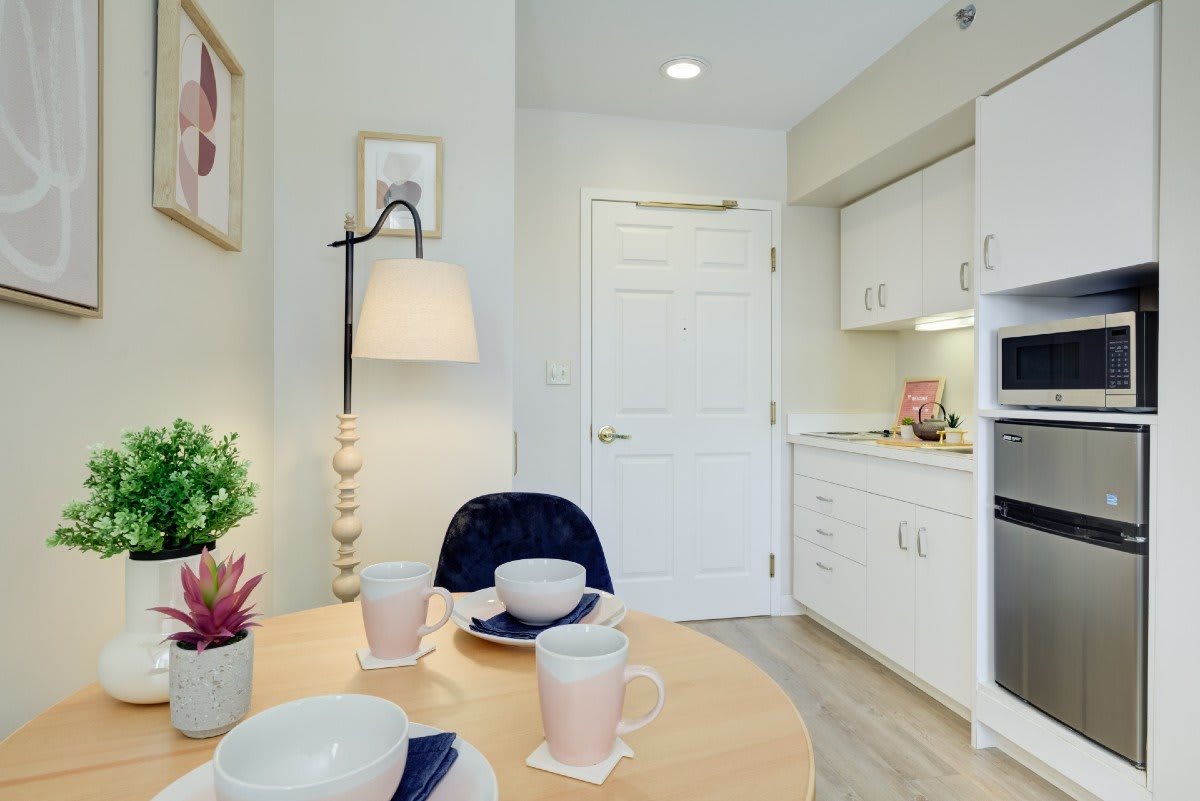 A cozy kitchen and dining area with a small table set for three, featuring a modern lamp and decorative plants.