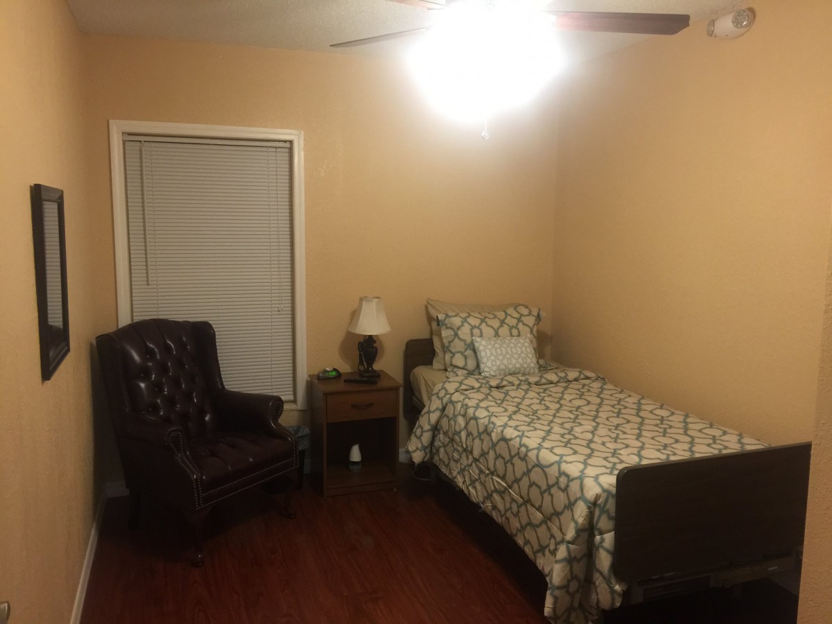 A simple bedroom with a single bed, armchair, and nightstand.