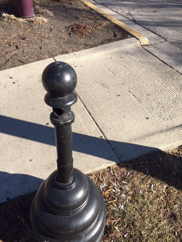 A black bollard standing on the edge of a sidewalk with shadows cast on the ground.