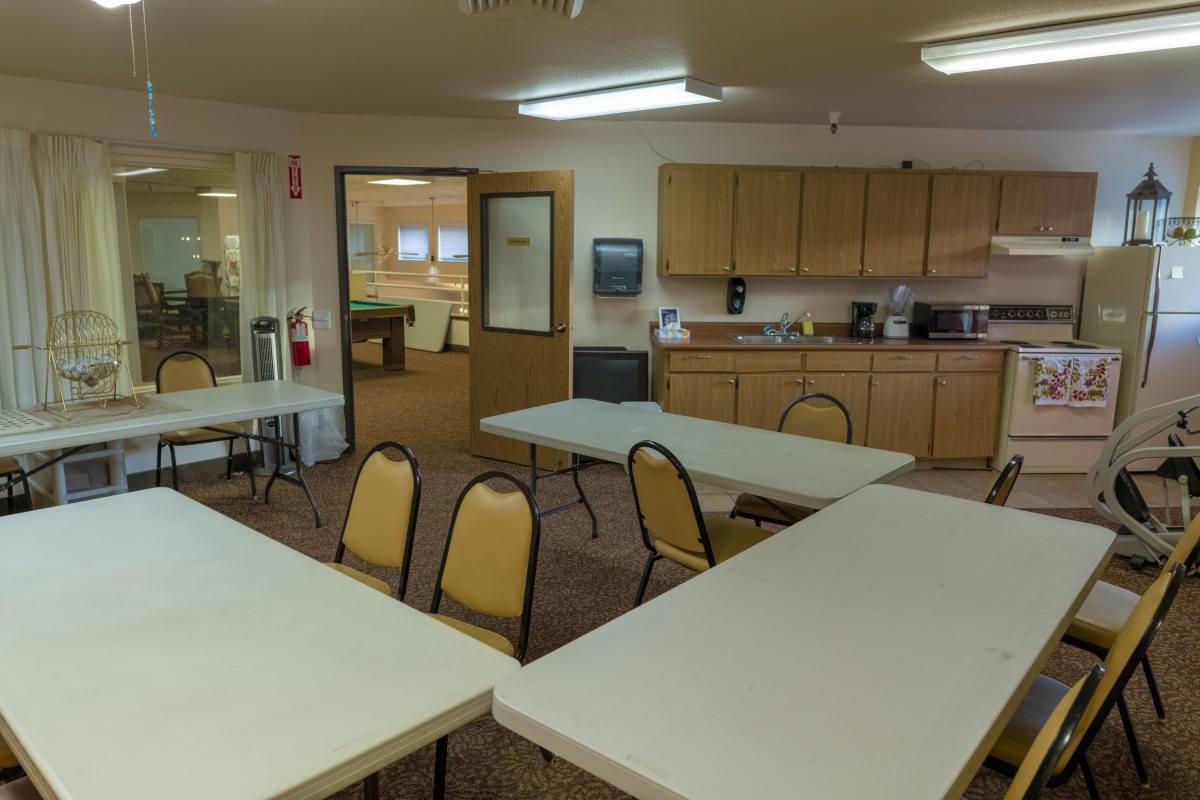 An office break room with tables and chairs, featuring a kitchenette area.
