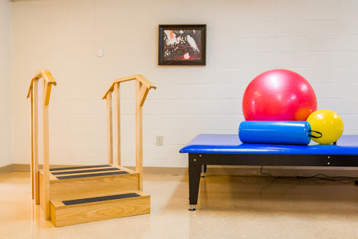 A rehabilitation space featuring a staircase for balance training, a blue treatment table, and a red exercise ball.
