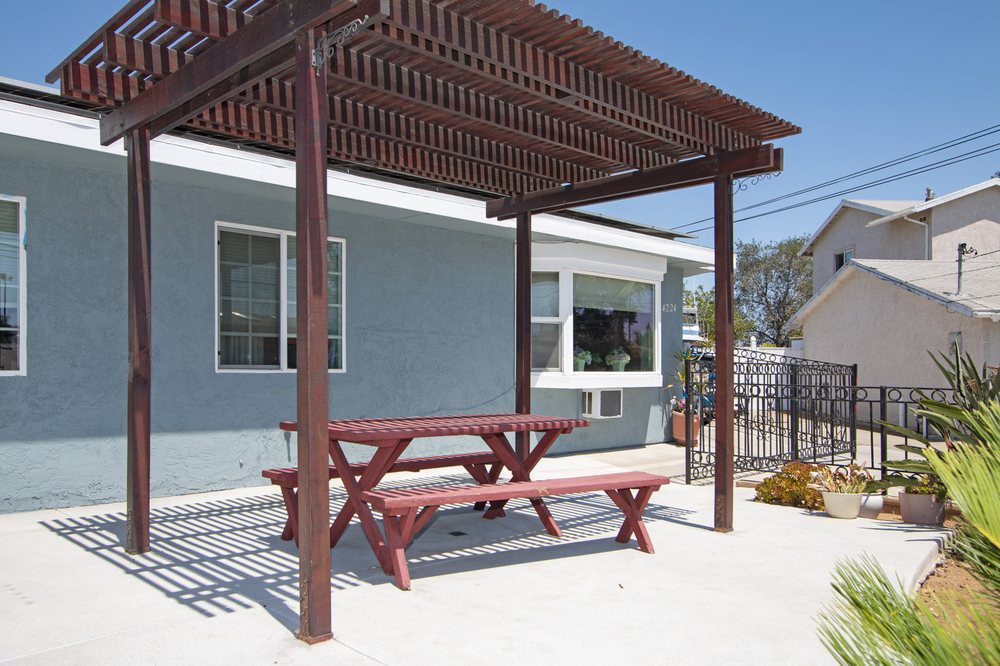 A backyard patio featuring a wooden pergola and red picnic table, providing a shaded outdoor seating area.