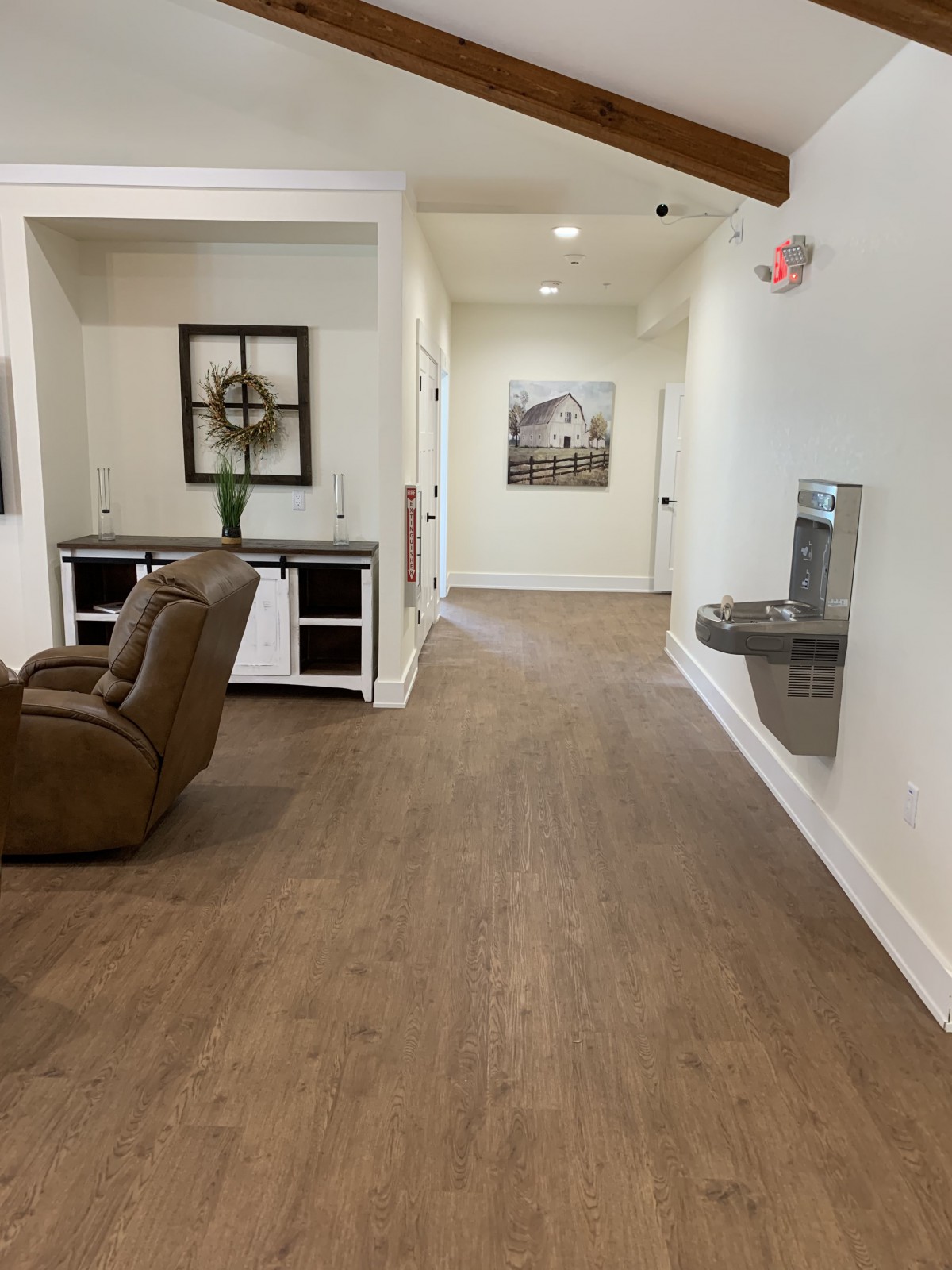 A hallway with wooden flooring, featuring a recliner and decorative items.
