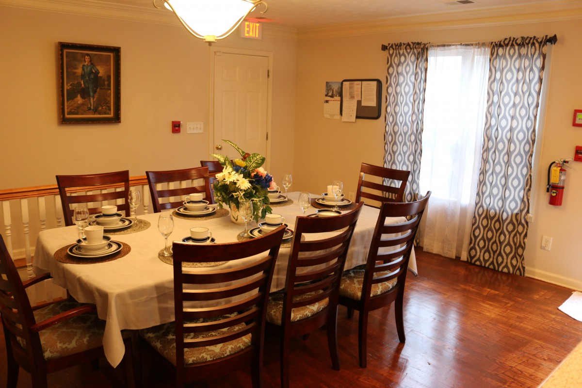 A dining room with a large table set for a meal, surrounded by wooden chairs and decorated with flowers.