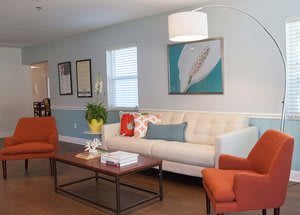 A modern living room with a beige sofa, orange armchairs, and contemporary artwork on the wall.