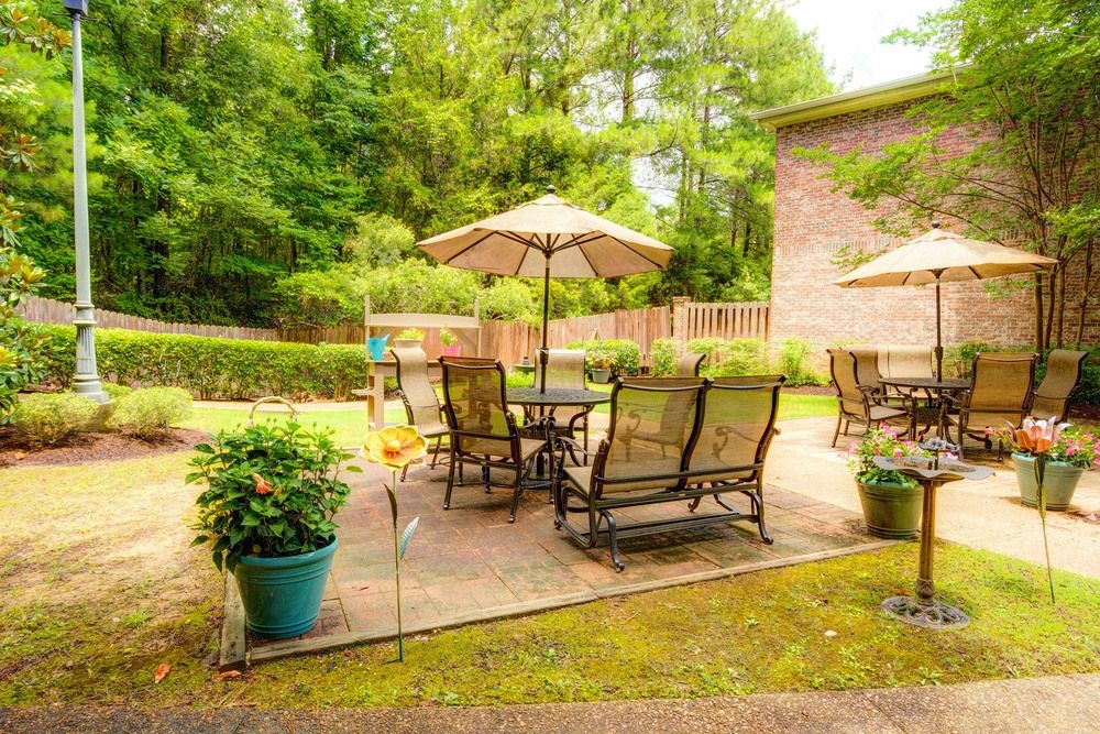 A cozy backyard patio with seating and an umbrella, surrounded by greenery.