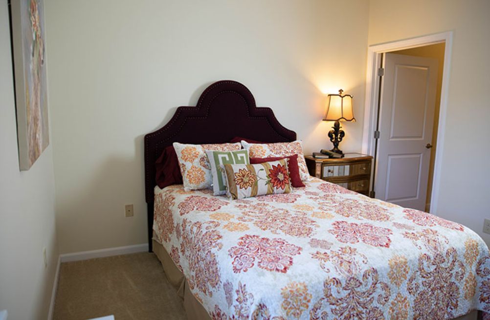 A cozy bedroom with a decorative bedspread and pillows, featuring a nightstand with a lamp.