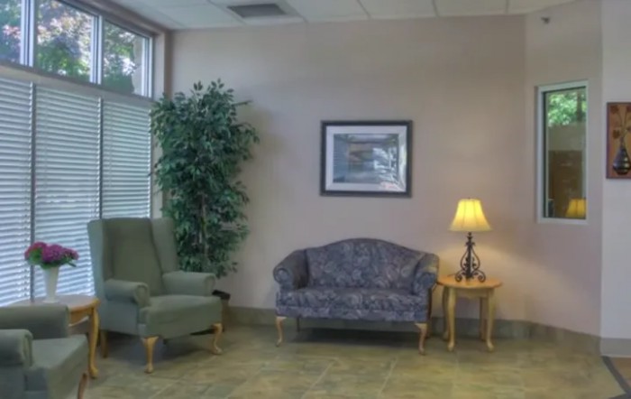 A cozy waiting room with a sofa, armchair, and a side table with a lamp.