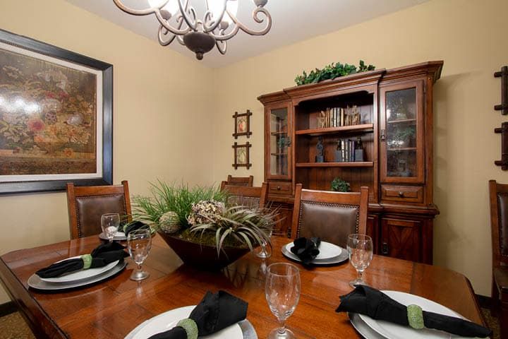 A cozy dining room with a wooden table set for guests, featuring elegant place settings and a classic chandelier.