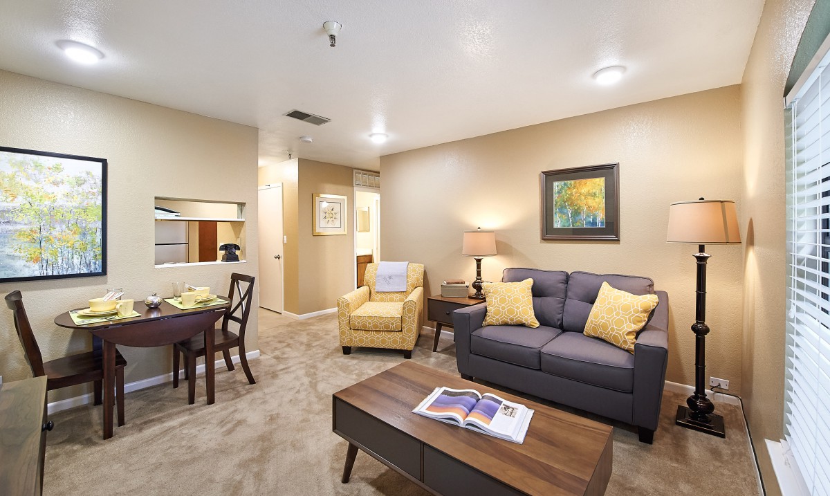 A cozy living room with modern furniture, including a sofa, armchair, coffee table, and dining area.